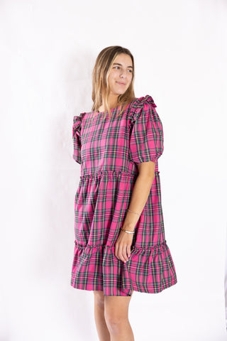 Woman wearing Belle Dress in pink plaid with playful puff sleeves, festive winter look.