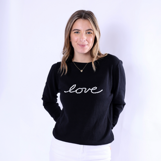 Woman wearing Celia Slim Fit Sweater with pearl “LOVE” script, styled with white pants.