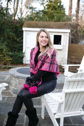 Model sitting outdoors wearing Claire Plaid Wrap in pink plaid layered over black outfit.