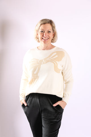 Cream Sweater Image: Woman wearing cream Madeline Holiday Bow Sweater with gold bow detail – festive winter pullover.