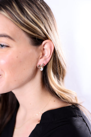 Close-up of woman wearing gold bow earrings with pearl accent, styled with a black top.