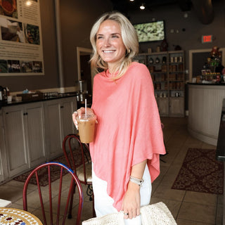 Women wearing watermelon colored poncho holding a bag and coffee