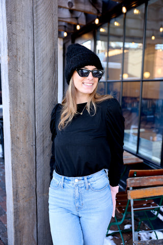 Woman wearing a black beanie and black puff sleeve top with jeans