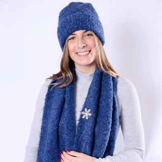 Image 2 (blue hat + scarf set with snowflake brooch): Woman in blue Poppy Hat and scarf accented with a snowflake brooch, smiling in cozy knitwear.