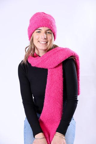 Woman wearing a bright pink knitted hat and scarf on a white background