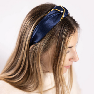 Model wearing navy Lanie Headband – Woman smiling in navy satin Lanie Headband with gold trim and knotted top design.