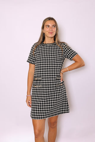 Woman wearing a black and white checkered dress against a light pink background