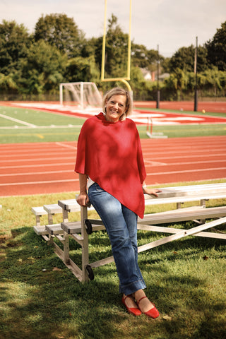 Woman in a red poncho sitting on bleachers at a sports field