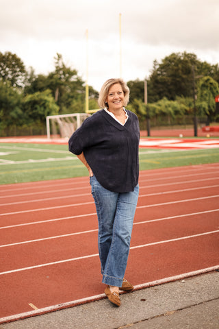 Woman standing on a track field wearing a dark sweater and jeans.