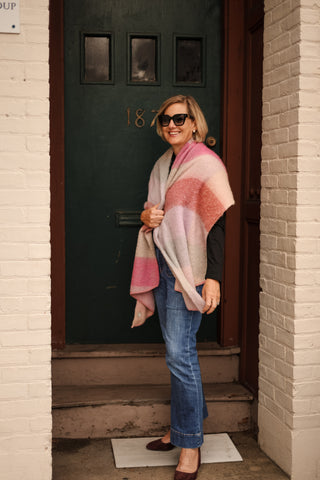 Woman standing outdoors wearing the Anne Scarf in pink stripes, draped as a wrap for a stylish fall look.
