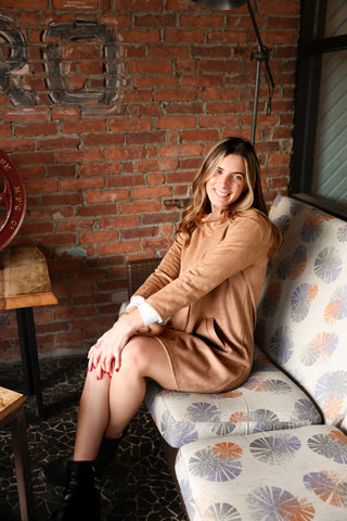 Woman sitting in camel faux suede Hilary Dress with turtleneck and pockets – chic, soft, and comfortable fall and winter dress.
