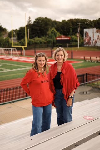 Women wearing black and red colors standing in front of a baseball field