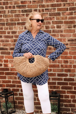 Woman wearing a tunic while holding a bag and wearing white pants