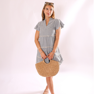 Woman in blue and cream striped dress holding natural colored woven half circle handbag 