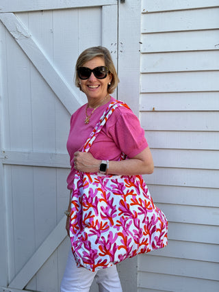 Woman wearing pink sweater and holding a pink and orange  watercolor coral print bag against a white background