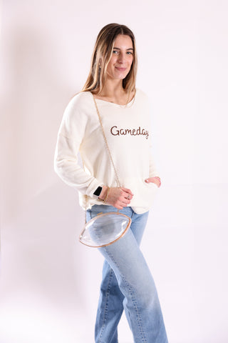 woman wearing a gameday sweater modeling a clear or stadium friendly football bag with gold cross body strap
