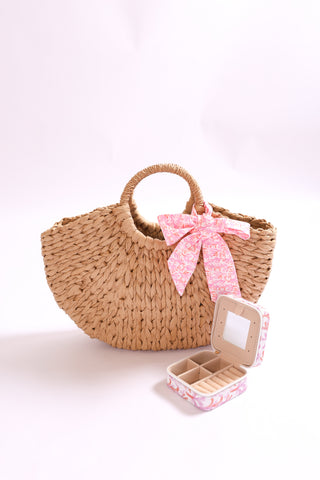 Natural colored woven half circle handbag accented with pink twillie on handle and displayed with coordinating travel jewelry box.