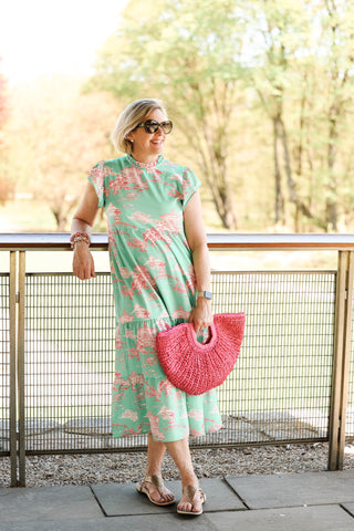 Woman in a floral dress holding a pink bag on a wooden deck.