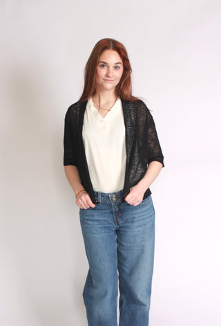 Woman wearing a black short sleeve cardigan paired with a white tank top and jeans