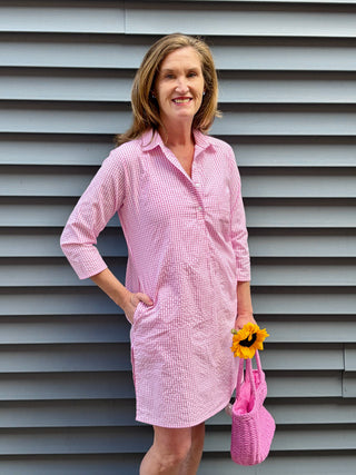 Woman in a pink checkered dress standing against a gray wall