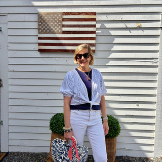 Woman wearing a white eyelet wrap, standing in front of a wooden American flag on a white building