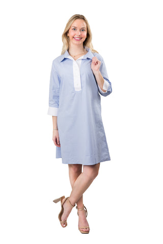 A woman wearing light blue tunic dress with white trim. The dress has three-quarter sleeves and a straight cut.