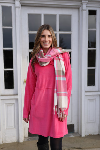 Woman wearing a pink dress and plaid scarf standing in front of a white door.