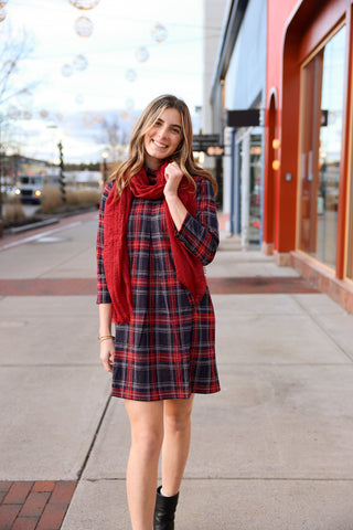 Woman wearing a plaid dress with a red scarf on a city street.