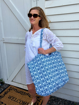 Woman wearing white eyelet lace tunic and holding a blue and white floral print bag against a white background