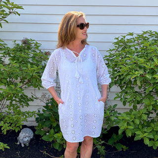 Woman wearing the Shift Style Eyelet Cover-Up in white with tie neckline and 3/4 puff sleeves, standing in a garden area.