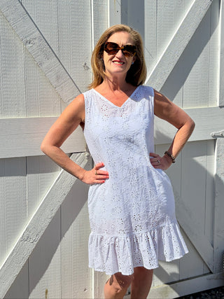 Woman wearing white ruffle trim mini eyelet cover-up with V-neck and drop waist, next to a white barn door.