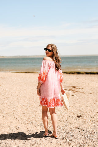 Woman in a pink dress standing on a beach with ocean in the background