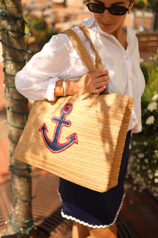 Person holding a straw bag with an anchor design outdoors