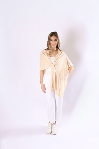 Woman wearing a sand colored wrap over a white top and pants on a white background