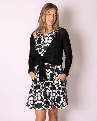 Model wearing the Kara Knit tie front cardi sweater wrap in black, styled over a black and white floral dress.
