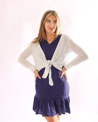 Model wearing the Kara Knit Wrap in silver, layered over a navy ruffle dress.