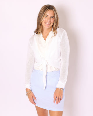 Model wearing the Kara Knit Wrap in white, tied at the waist over a light blue striped skirt.