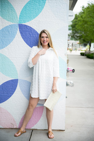 Woman in a white dress standing in front of a colorful circular patterned wall.
