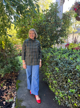Woman standing outdoors in a garden setting wearing a plaid shirt with ruffle neck, 3/4 sleeves and tie back