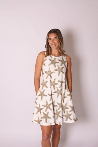 Woman wearing sleeveless A-line dress with pockets in tan and white sequins starfish print