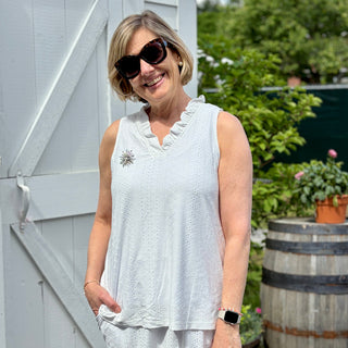 Woman in a light dress standing outdoors near a wooden shed and barrel.