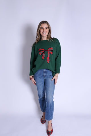 Woman wearing green Christmas sweater with red tartan bow design.