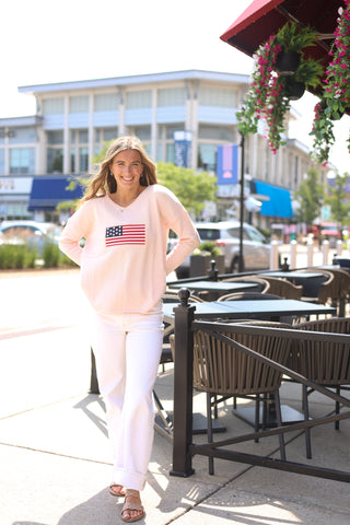 Woman in a pink sweatshirt with an American flag design standing outdoors 
