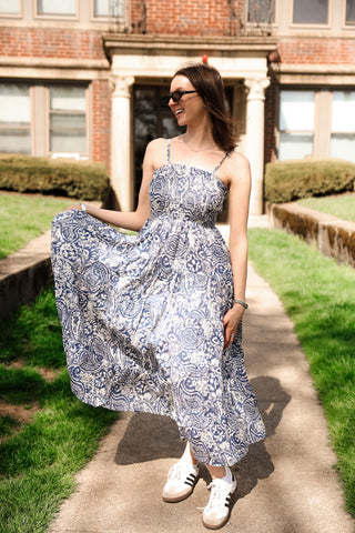 Woman in a patterned dress standing on a sidewalk with a building in the background