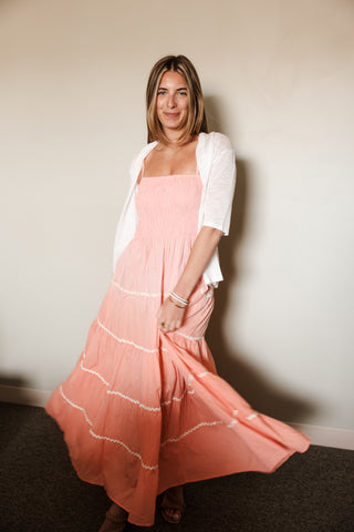 Woman wearing a pink dress with white stripes against a plain wall.