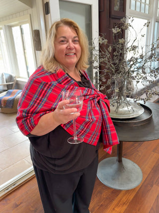 Woman in a red tartan plaid keyhole shawl holding a glass of wine indoors.