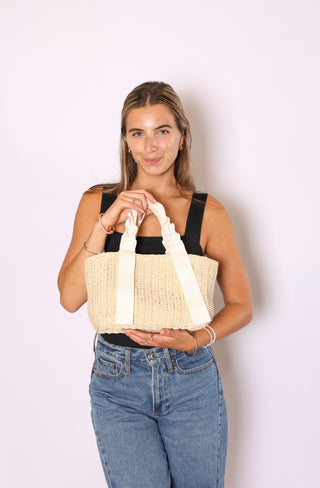 Woman holding a cream woven handbag 