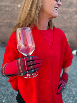 Person wearing a red sweater and plaid gloves holding a glass of red wine.