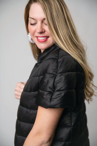Woman wearing a black puffer vest against a plain background