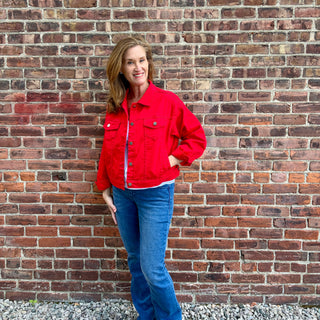 Women wearing red jean jacket and  blue jeans standing in front of a brick wall